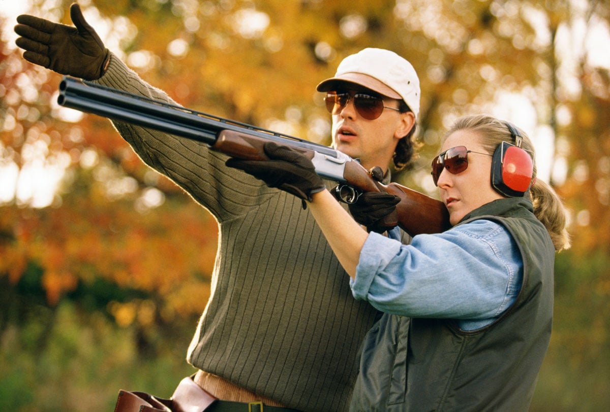 woman holding hunting rifle with man instructing 